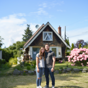 A young couple stands in front of their A frame home illustrating affordable elegance in a suburban setting.